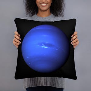 May include: A square throw pillow featuring a deep blue, spherical depiction of the planet Neptune centered against a solid black background. The planet graphic displays subtle variations in blue tones and cloud-like atmospheric bands.
