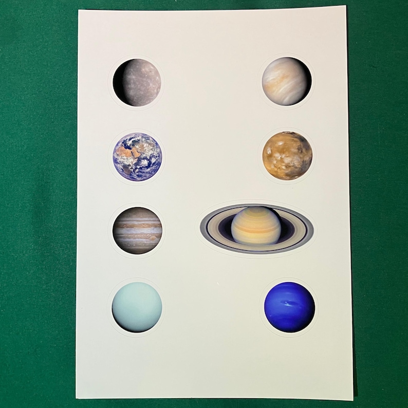 May include: A white rectangular sheet featuring eight circular stickers of planets. The stickers display Mercury, Venus, Earth, Mars, Jupiter, Saturn with its rings, Uranus, and Neptune in a two-column arrangement on the paper surface.