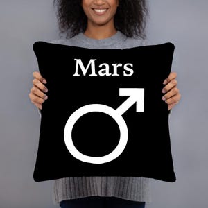 May include: A square black throw pillow featuring the white text Mars centered above a large white Mars planetary symbol. The design is printed on the front of the pillow, which has a smooth, solid black fabric finish throughout.