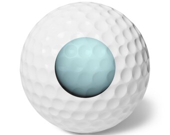 May include: A white golf ball with a dimpled surface texture featuring a large, circular, light blue graphic element centered on the front. The sphere has a smooth, rounded shape with a consistent pattern of small, circular indentations.
