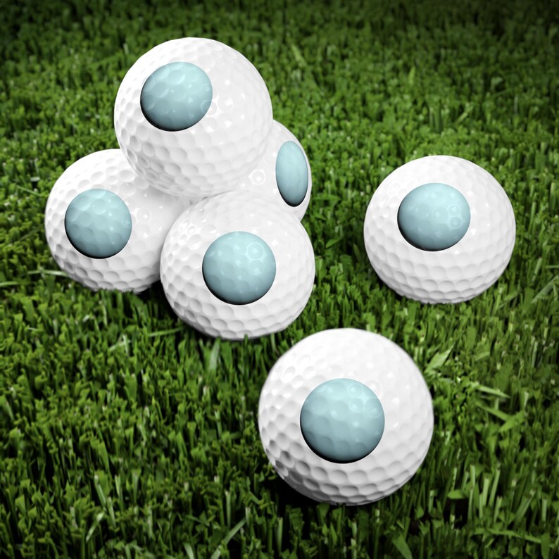 May include: A collection of five white golf balls, each featuring a smooth, light blue circular inlay on its surface. The golf balls have a dimpled texture and are arranged in a cluster, with four balls stacked together and one positioned separately.