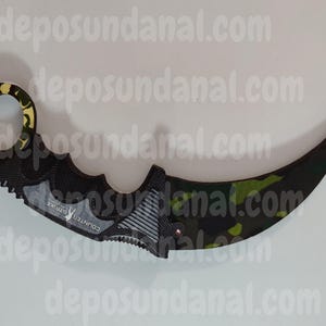 Könnte beinhalten: Ein schwarzes und grünes Tarnmuster-Karambit-Messer mit einem gelben und schwarzen Griff. Das Messer hat eine gezahnte Klinge und der Text "COUNTER STRIKE" ist auf der Seite aufgedruckt.