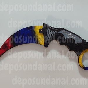 May include: A black and grey karambit knife with a red, yellow, and blue handle. The knife has a finger ring and the words "COUNTER STRIKE" are printed on the handle.