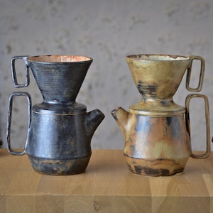 Może przedstawiać: Dwa ceramiczne ekspresy do kawy z pasującymi pokrywkami. Jeden jest ciemnoniebieski, drugi brązowy i beżowy. Oba mają uchwyt i wylewkę. Ekspresy do kawy stoją na drewnianej powierzchni.