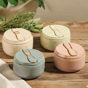 Può includere: Quattro saliere in ceramica color crema, verde, blu e rosa. Ogni contenitore rotondo ha un coperchio abbinato con un cucchiaio integrato. Le saliere sono macchiate e poggiano su una superficie di legno, adatte per la cucina o la sala da pranzo.