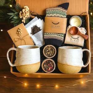Pode incluir: Uma caixa de presente com itens relacionados ao chá. Inclui duas canecas brancas e amarelas, duas latas de chá, um par de meias estampadas, uma vela e uma colher de pau. Um pequeno cartão e saquinhos de chá também estão incluídos.