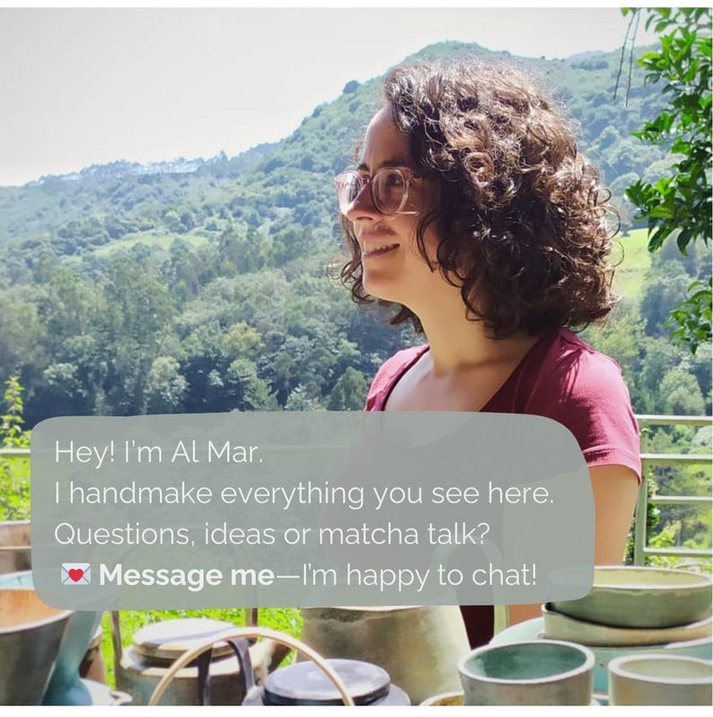 May include: A woman with curly brown hair and glasses smiles, set against a backdrop of lush green hills. Text overlay reads: "Hey! I'm Al Mar. I handmake everything you see here. Message me&mdash;I'm happy to chat!"