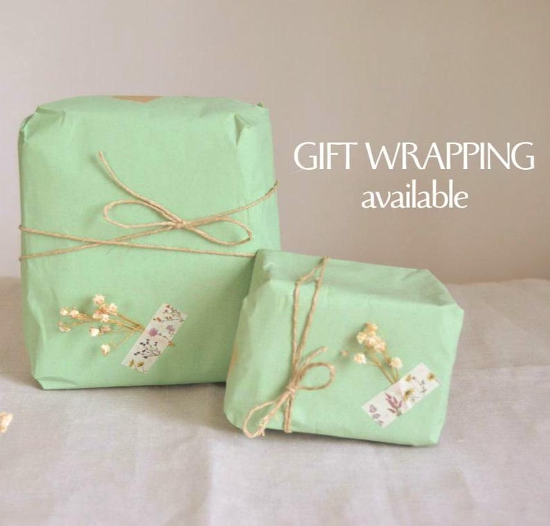 May include: Two gifts wrapped in pale green paper, tied with twine bows. Each package is decorated with dried flowers and a decorative sticker. The text "GIFT WRAPPING available" is visible in the background.