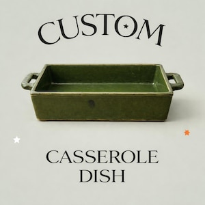 May include: An olive green rectangular casserole dish with handles. The words "CUSTOM" and "CASSEROLE DISH" are displayed above and below the dish. The dish is empty and set against a neutral background.