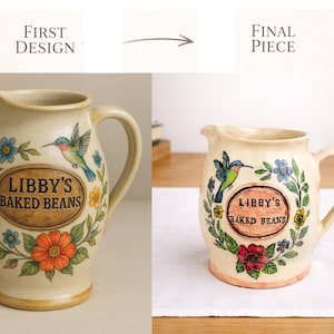 May include: Cream-coloured ceramic jug with a handle and spout, decorated with a floral and hummingbird design. The jug has the text "LIBBY'S BAKED BEANS" in an oval frame. The design includes blue, orange, and yellow flowers, and green leaves.