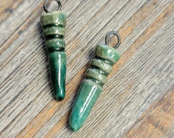 May include: Two green ceramic pendants with black accents and a silver loop for hanging.
