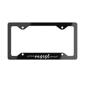 May include: A black car number plate frame with the word "resist" in a white, cursive font. The frame is rectangular with rounded corners and four mounting holes.
