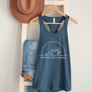 May include: A dark blue tank top with a white graphic of a mountain range and a sun. The text "FOXTROT DELTA TANGO" is printed below the graphic.