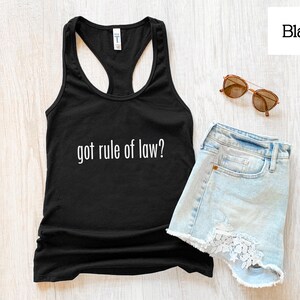 May include: A black racerback tank top with the white text "got rule of law?" printed on the front, paired with light blue denim shorts featuring white lace trim and a pair of brown-tinted sunglasses with thin gold-tone metal frames.