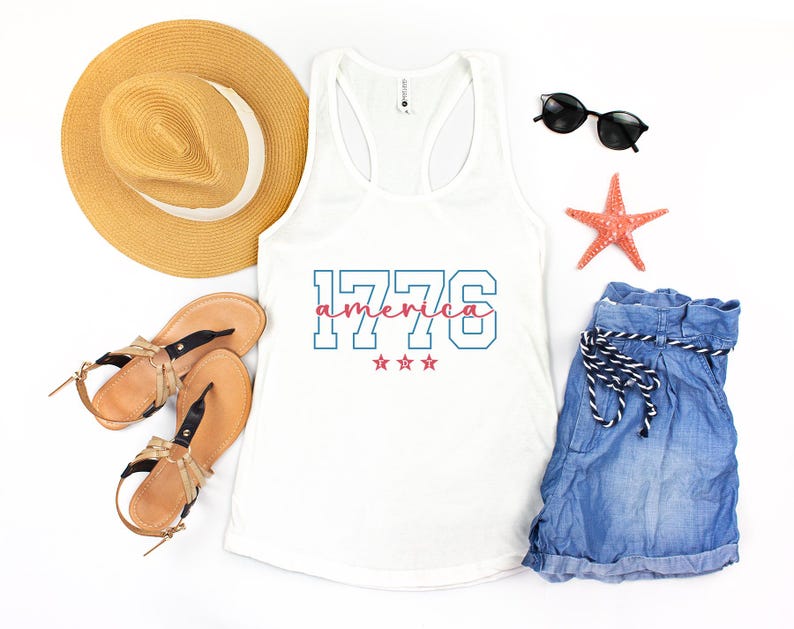 May include: A white vest top with the text "1776 america" in blue and pink, with three pink stars. The image also includes a straw hat, sunglasses, denim shorts, sandals, and a starfish.