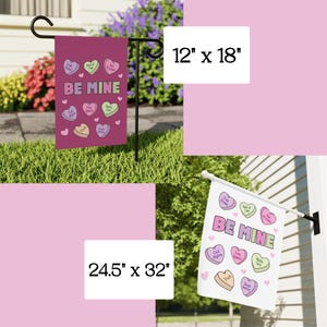 May include: A set of two garden flags, one measuring 12" x 18" and the other 24.5" x 32". Both flags are magenta with the words "BE MINE" and heart-shaped candies with phrases like "Free Press" and "Civil Rights".