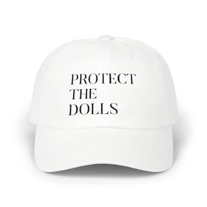 Puede incluir: Gorra de béisbol blanca con texto negro que dice "PROTECT THE DOLLS".