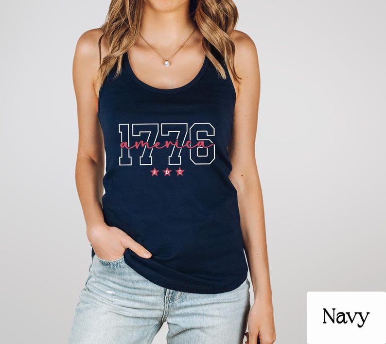 May include: A navy blue vest top featuring the text "1776 america" in white and pink. The design includes three pink stars. The top is a casual style.