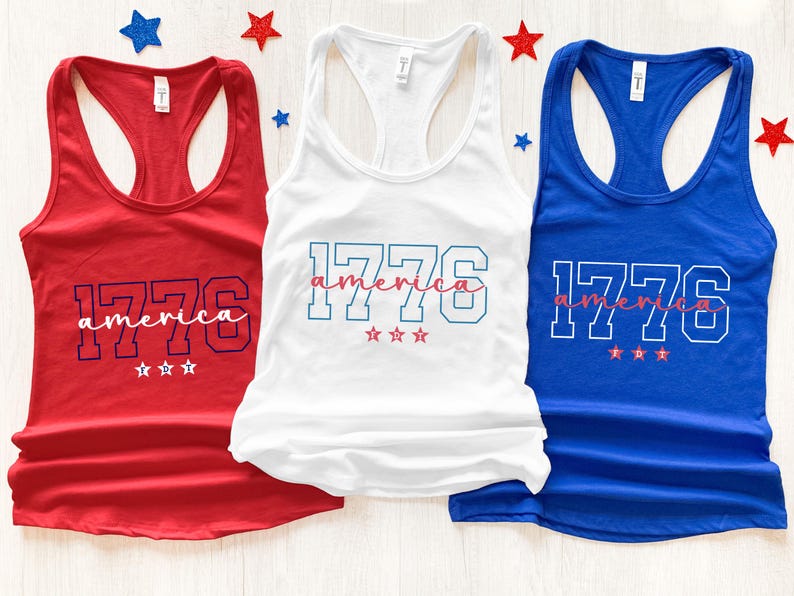 May include: Three tank tops in red, white, and blue. Each top has the number "1776" in a block font, with the word "america" in a script font underneath. Three small stars are below the text on each tank top.