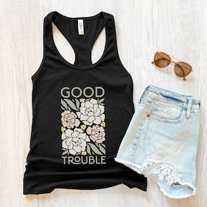 Può includere: Canotta nera con un design floreale e il testo "GOOD TROUBLE" stampato sul davanti.