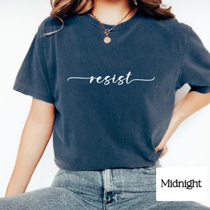 May include: A navy blue t-shirt with the word "resist" written in white cursive script.