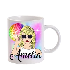 May include: White ceramic mug with a colourful design featuring a woman with blonde hair wearing sunglasses and a disco ball. The mug has the name "Amelia" written on it.