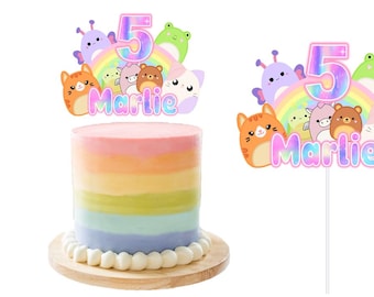 以下が含まれることがあります： ピンク、パープル、ブルーのグラデーションデザインのレインボーケーキトッパー。トッパーには、数字の5、レインボー、さまざまな漫画の動物が描かれています。トッパーには「Marlie」というテキストが含まれています。