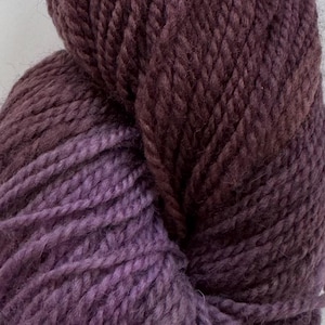 Peut inclure: Gros plan d'une pelote de laine aux tons violets et bordeaux. La laine est épaisse et texturée, avec un léger dégradé du violet clair au bordeaux foncé. Idéale pour les projets de tricot ou de crochet.