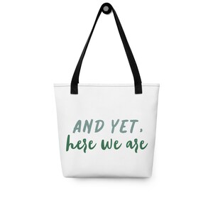 May include: White tote bag with black handles and the text "AND YET, here we are" in green and blue lettering.