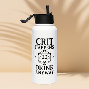 May include: White water bottle with a black lid and straw. The bottle has the text "CRIT HAPPENS" above a graphic of a 20-sided die, with the words "DRINK ANYWAY" below. The bottle is designed for cold beverages.