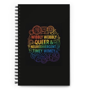 Könnte beinhalten: Schwarzes Spiralnotizbuch mit einem Regenbogenmuster. Das Design enthält die Worte "Wibbly Wobbly Queer & Neurodivergent Timey Wimey" in einem kreisförmigen Muster. Das Notizbuch hat leere Seiten.