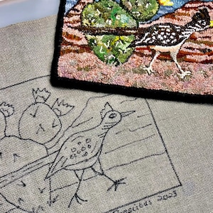 May include: A close-up of a needlepoint canvas with a black and white line drawing of a bird and cactus. The canvas is labeled "J. Janine Boscius 2003".