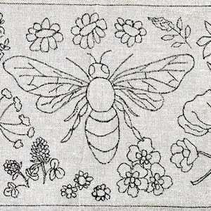 May include: Embroidered design of a bee and flowers on a light grey fabric. The black outline depicts a bee in the centre, with various floral elements around it, creating a rustic, handmade aesthetic.