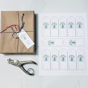 May include: A wrapped gift in brown paper with a tag that says "Oh Christmas Tree" and "Emmie Mom + Dad". The tag is tied with black and white twine and red and white twine. A sheet of printable gift tags is next to the gift.