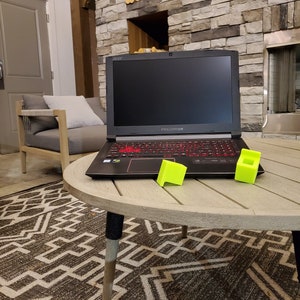 May include: A black Acer Predator laptop computer with a red backlit keyboard is on a wooden table with two yellow blocks. The laptop is in front of a stone fireplace.