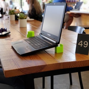 May include: A black laptop computer with a green block on each side of the keyboard. The laptop is open and sitting on a wooden table with a black table number that says "49".