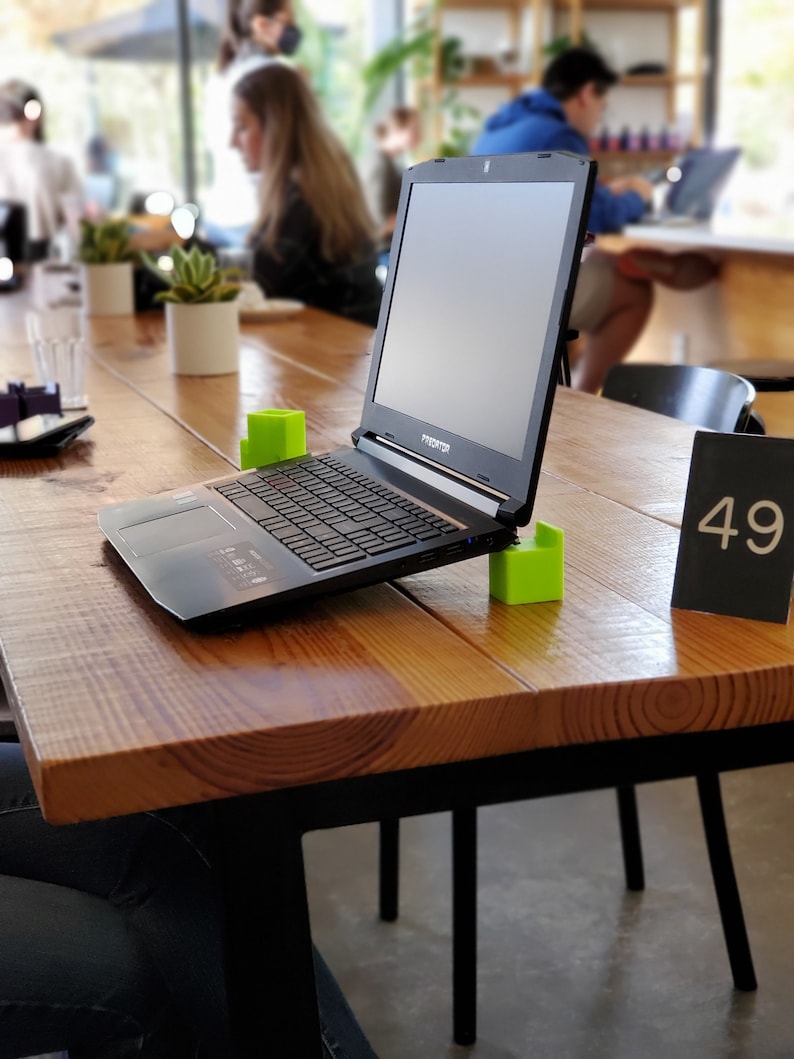 May include: A black laptop computer with a green block on each side of the keyboard. The laptop is open and sitting on a wooden table with a black table number that says "49".