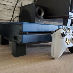 May include: A blue and black gaming console with a white and gold controller. The console is sitting on a wooden surface.