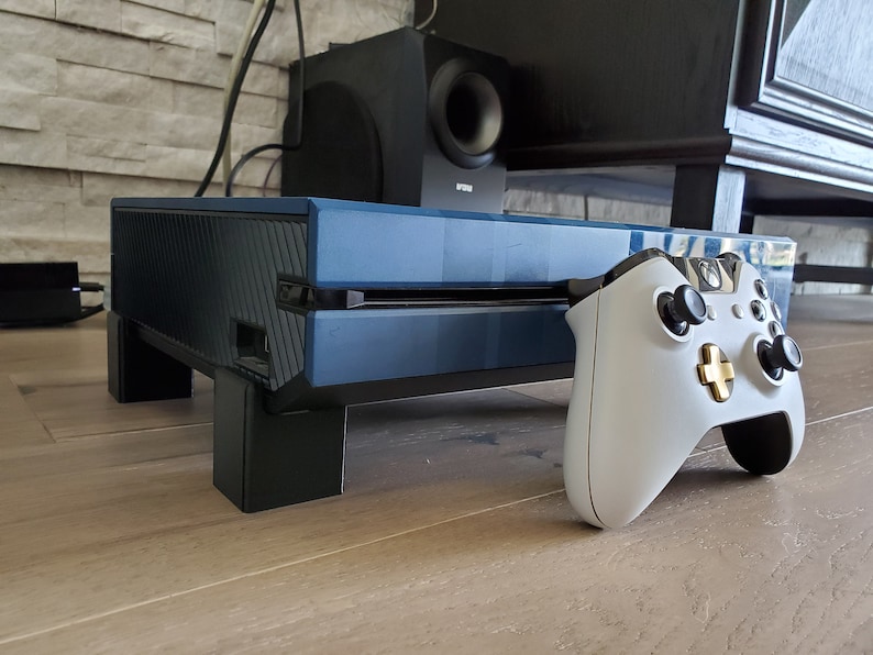 May include: A blue and black gaming console with a white and gold controller. The console is sitting on a wooden surface.
