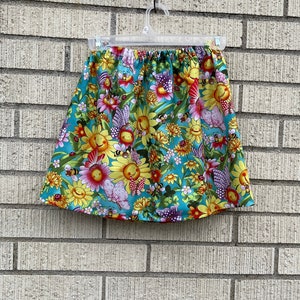 May include: A turquoise skirt with a floral print featuring yellow sunflowers, pink flowers, butterflies, and bees.