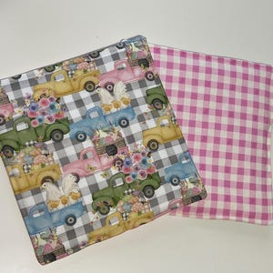 May include: Two fabric squares, one with a checkered pattern in black and white and a repeating pattern of vintage trucks with flowers and chickens, and the other with a pink and white gingham pattern.