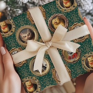 May include: A wrapped gift with green wrapping paper featuring framed cat portraits. The gift is tied with a cream-colored ribbon and bow. The background includes a snowy Christmas tree.