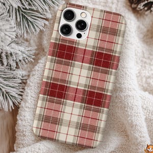 May include: A phone case with a red, white, and brown plaid pattern. The case has a camera module with multiple lenses. The background includes a white, textured surface and a pine branch.