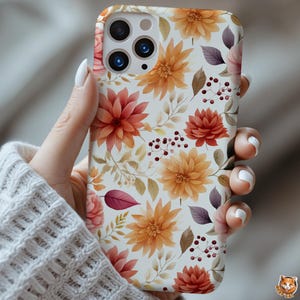 May include: A floral phone case featuring a repeating pattern of orange, red, and pink flowers with green and brown leaves on a white background. The case has a glossy finish and is held by a hand.