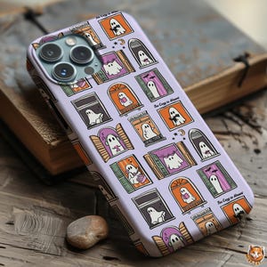 May include: A lavender phone case featuring a repeating pattern of cartoon ghosts in windows. The windows are in various colors, including orange, purple, and brown. The text "Too Cozy to Haunt" is printed on the case.