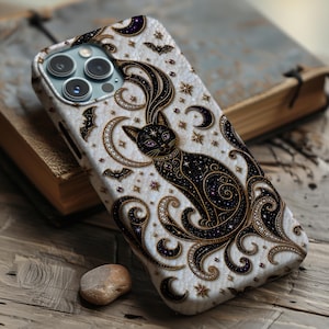 May include: A white phone case featuring a black cat illustration with purple eyes, surrounded by gold and black crescent moons, stars, and small bats. The design includes intricate swirling patterns and a textured appearance on the surface.
