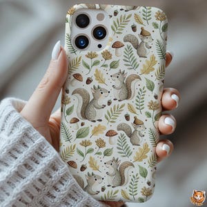May include: A phone case featuring a repeating pattern of cartoon squirrels, mushrooms, acorns, and leaves in shades of brown, green, and yellow on a cream background. The case has a glossy finish and a camera cutout.