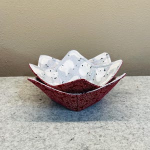 May include: Two fabric bowl cozies. The outer layer is a deep red with a white floral pattern. The inner layer is light gray with white polar bear designs. The cozies are nested together.