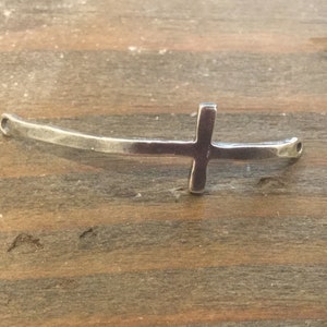 May include: Silver cross charm with a curved bar, suitable for jewelry making.