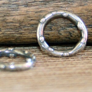 May include: Two silver jump rings with a textured, slightly bumpy surface. The rings are round and have a smooth, polished finish.